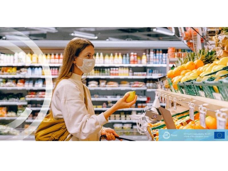 Kobieta w sklepie, z maseczką na twarzy, zastanawia się nad zakupem. W ręku trzyma cytrynę.